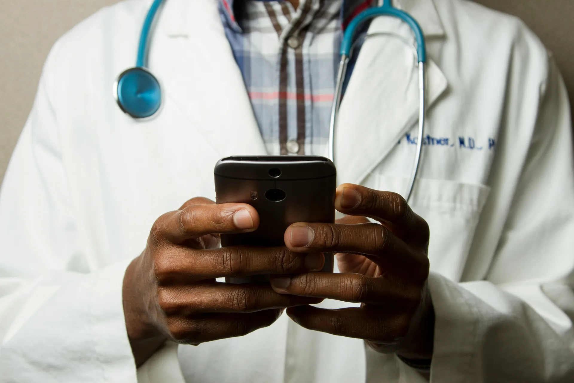 A physician in a white coat using a smartphone
